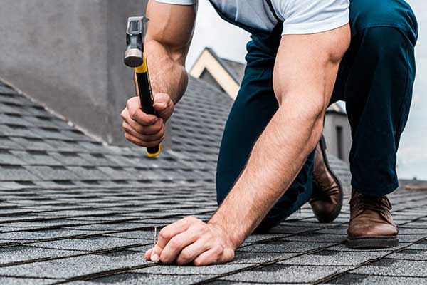 Close up of a worker repairing a gray shingle roof with a nail and hammer