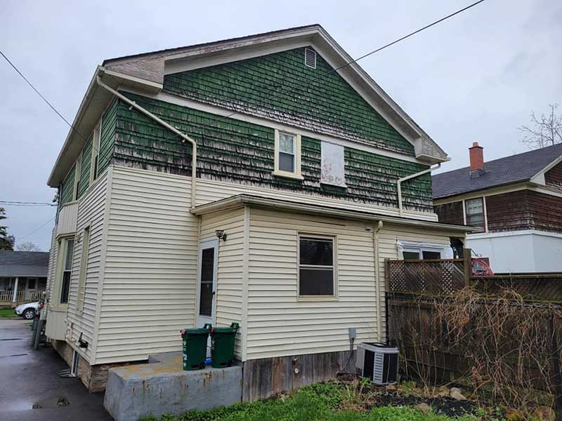 Small two-story home in the process of getting its visibly old green siding replaced with new beige vinyl siding